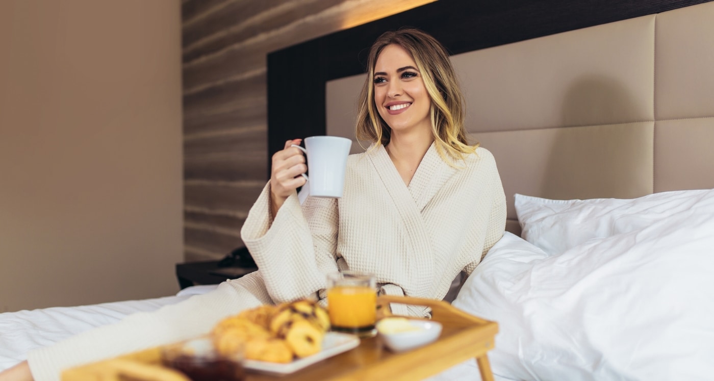 woman at a hotel having room service breakfast in bed saving money after reading the FoundersCard Review travel Benefits