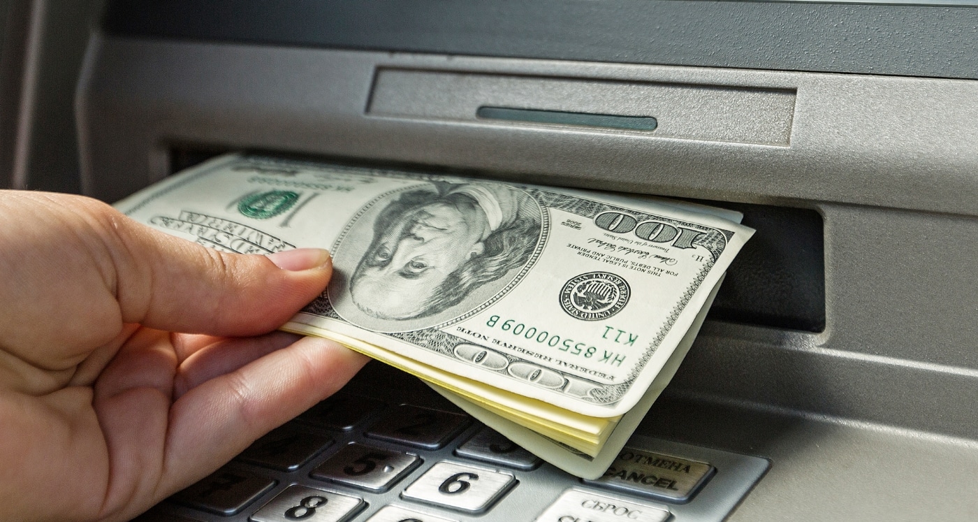 hand takes cash out of ATM understanding How to Withdraw Money From the Bank