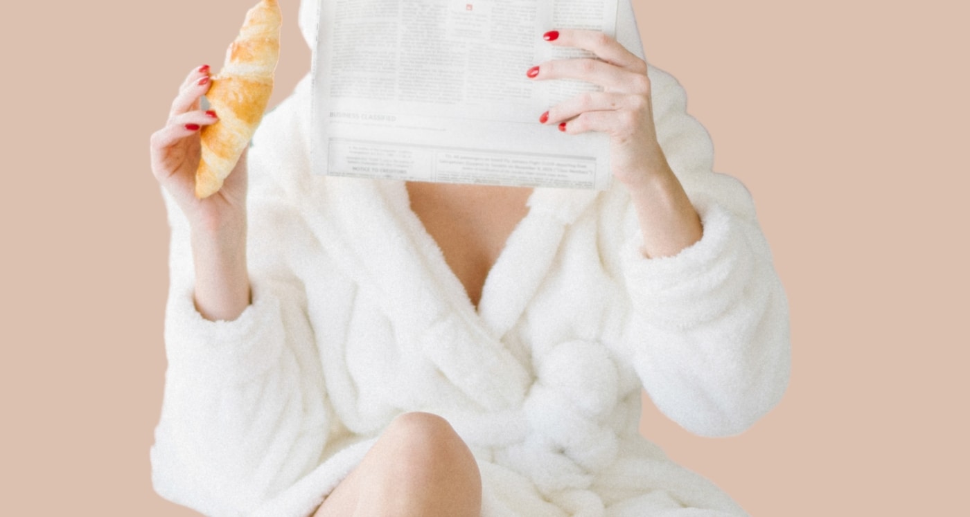 woman wearing loungewear and holding a croissant reads about Is Being Debt Free the New Rich?