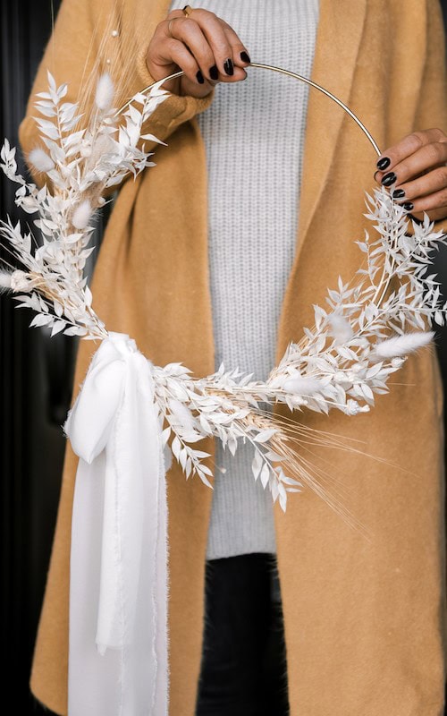 woman holds up the wreath she made as a Fall side hustle to make extra cash in Autumn