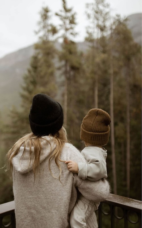 business owner Mom holds baby as she looks out to forest on a chilly October morning while planning her october content ideas