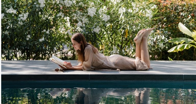 woman sits by pool reading about Why These 9 Uncomfortable Habits Are Actually Life’s Real Magic Pills